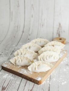 Gyozas de verduras crudas sobre una tabla de madera espolvoreada con harina.