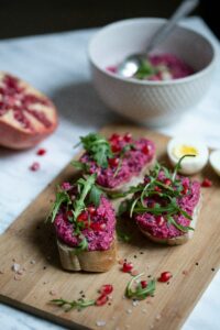 Tostas con hummus de remolacha, rúcula y granada sobre una tabla de madera.